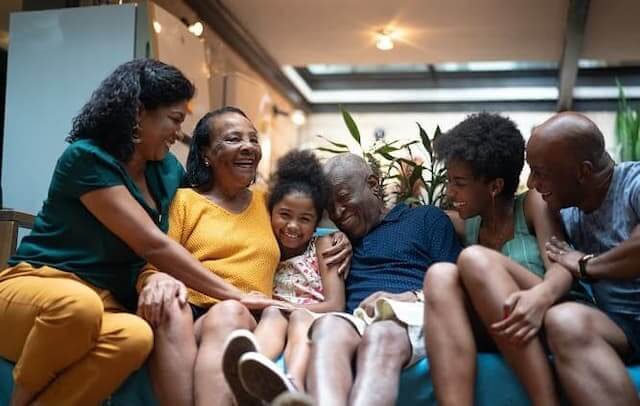 ma família negra de várias gerações abraçada sentada no sofá todos sorrindo em casa.