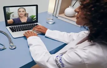 Foto de uma médica sentada na mesa fazendo uma videoconferência com outra médica através do laptop no consultório. e