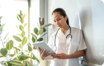 Foto de uma médica encostada na parede analisando uma ficha médica no consultório.