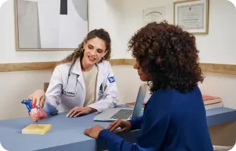 Foto de uma médica na mesa do consultório, realizando o atendimento de uma paciente.