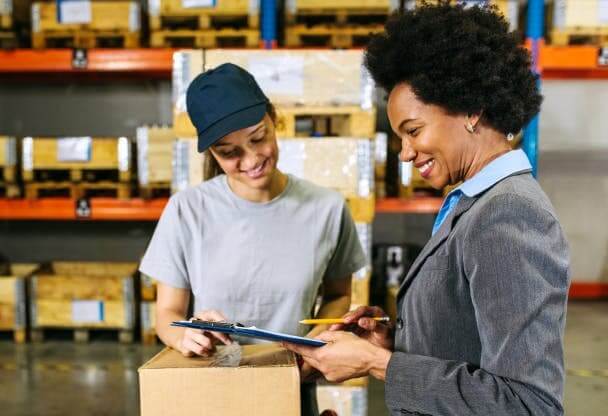 Foto de duas mulheres conversando e observando uma caixa de encomenda dentro de um centro de distribuição.